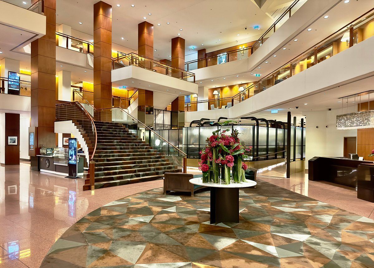 A large lobby of a hotel with stairs and a table with flowers on it.