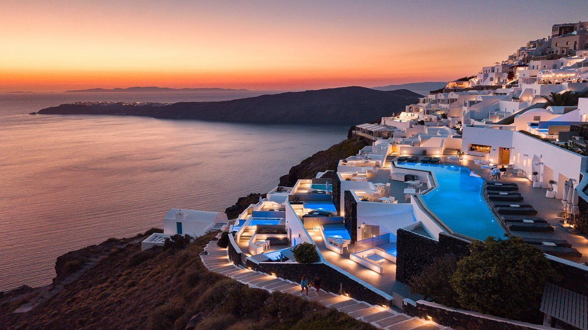 An aerial view of a hotel on a hill overlooking the ocean at sunset.