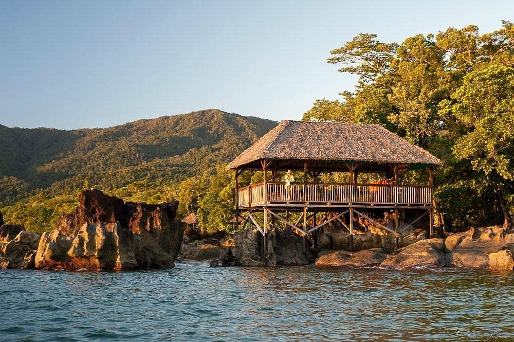 A small hut on stilts overlooking a body of water with mountains in the background.