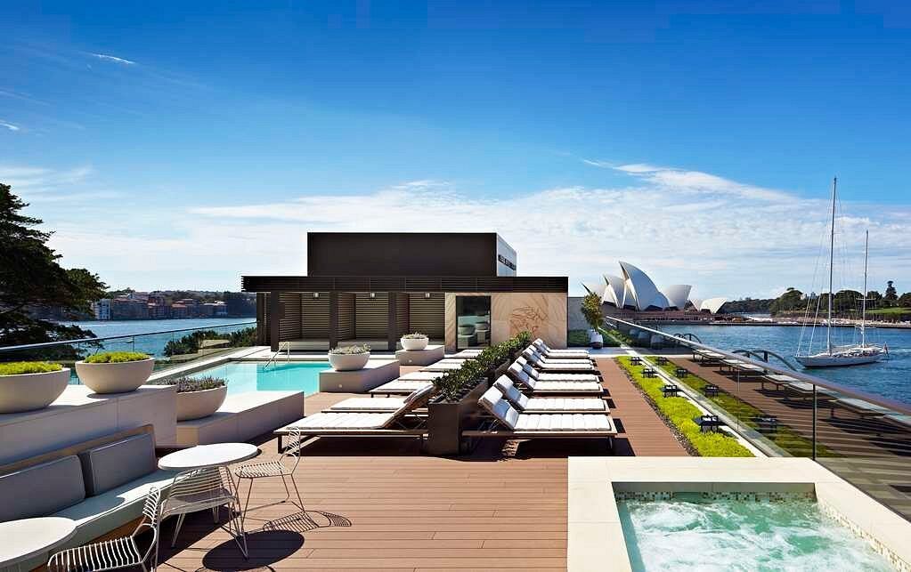 There is a swimming pool on the roof of a building overlooking the water.