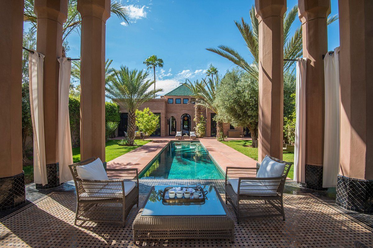 A patio with chairs and a table in front of a large swimming pool.