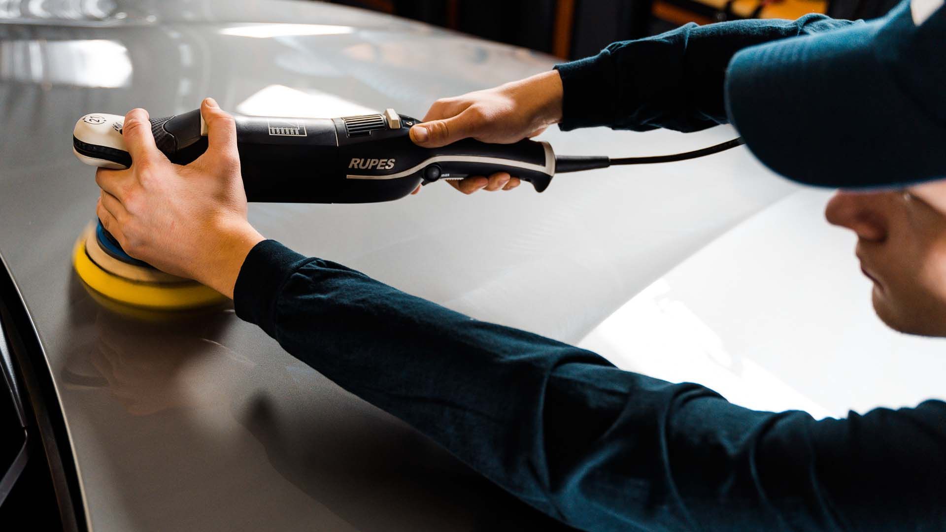 A man is polishing a car with a machine.