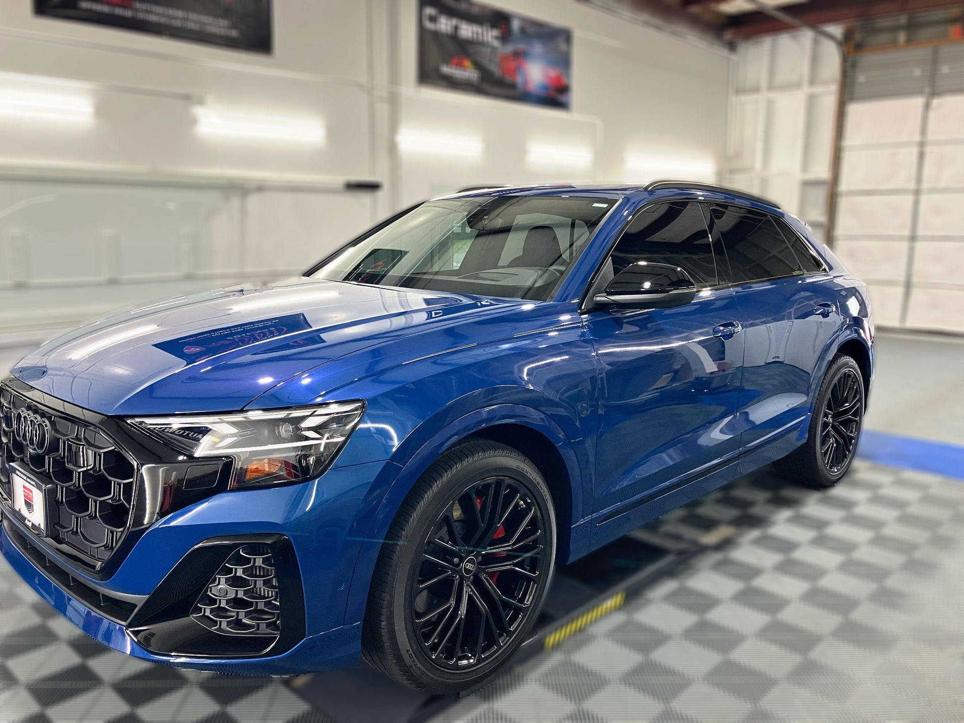 A blue car is parked in a garage with a checkered floor.