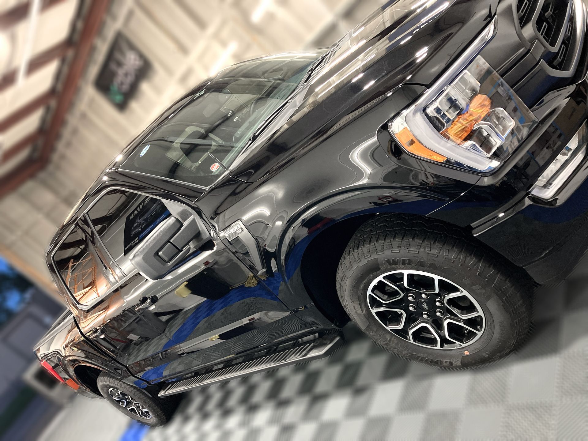 A black truck is parked on a checkered floor in a garage.