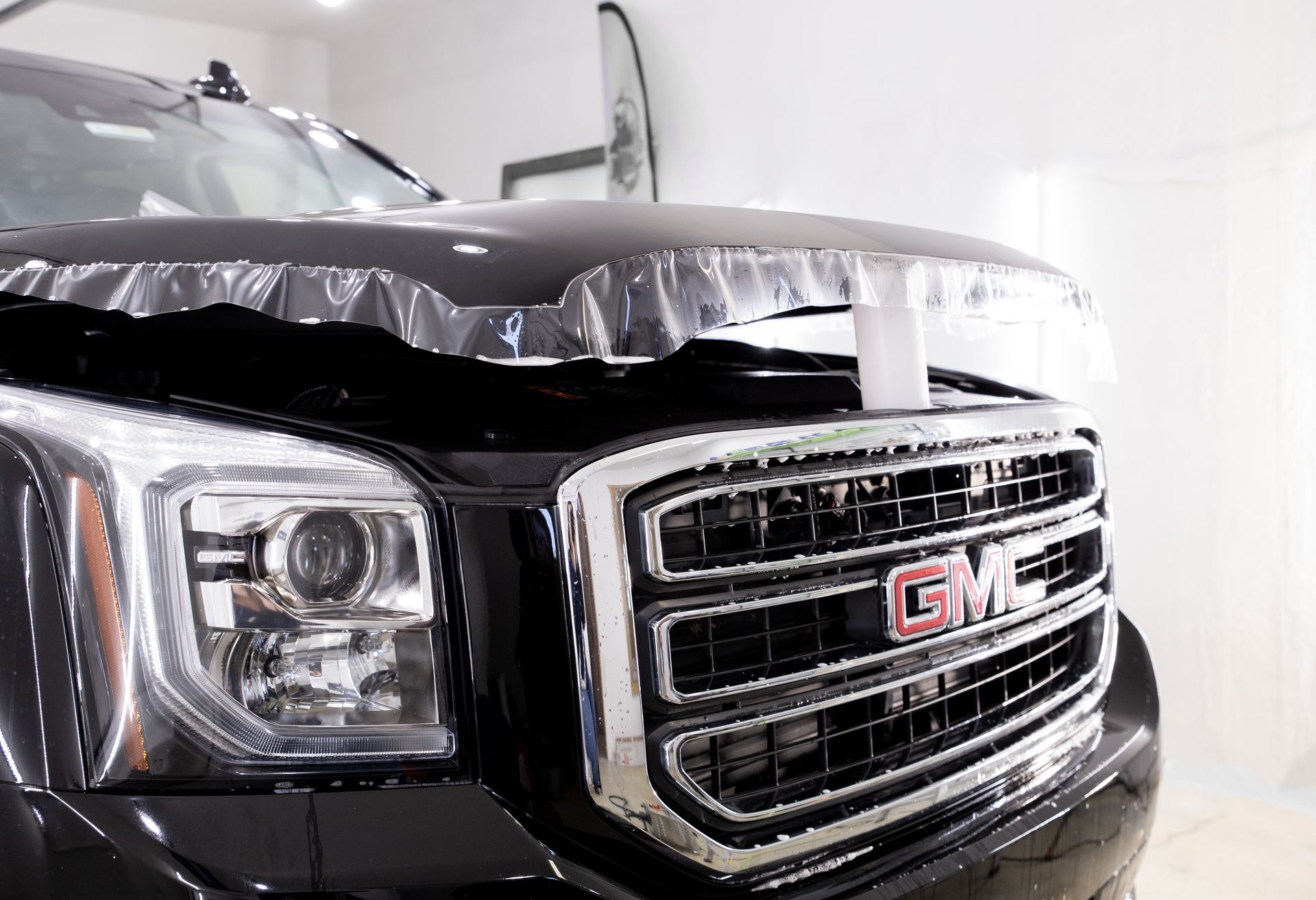 Damaged black GMC truck front end with hood bent open in a bright indoor garage