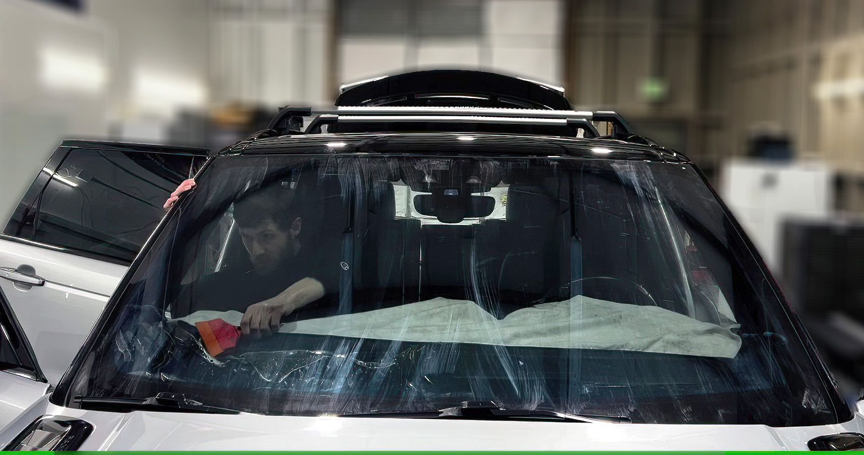 A man is cleaning the windshield of a car in a garage.