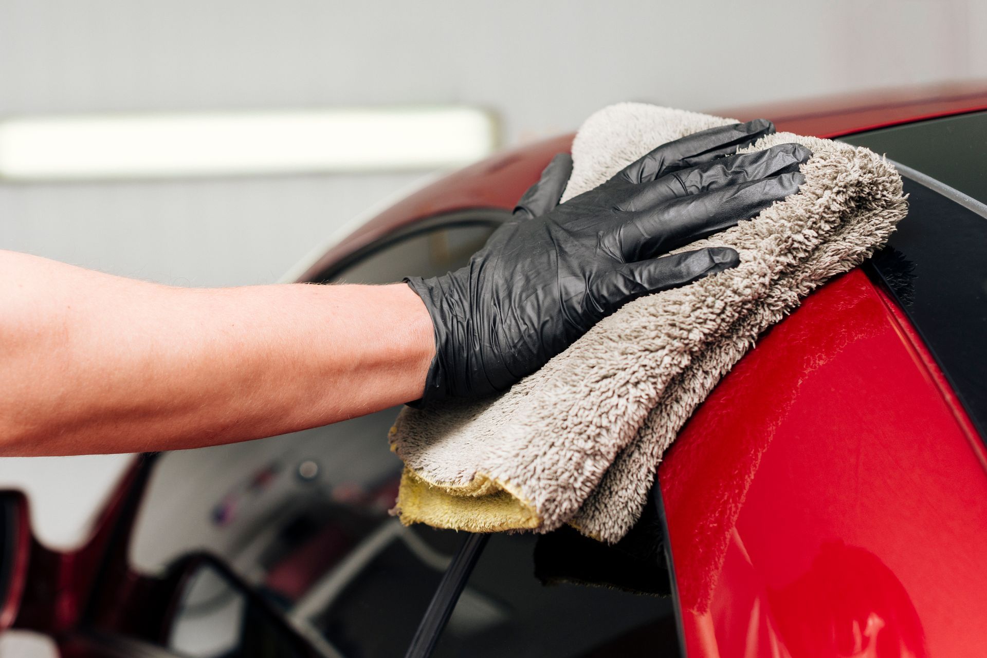 A person wearing black gloves is cleaning a red car with a towel.