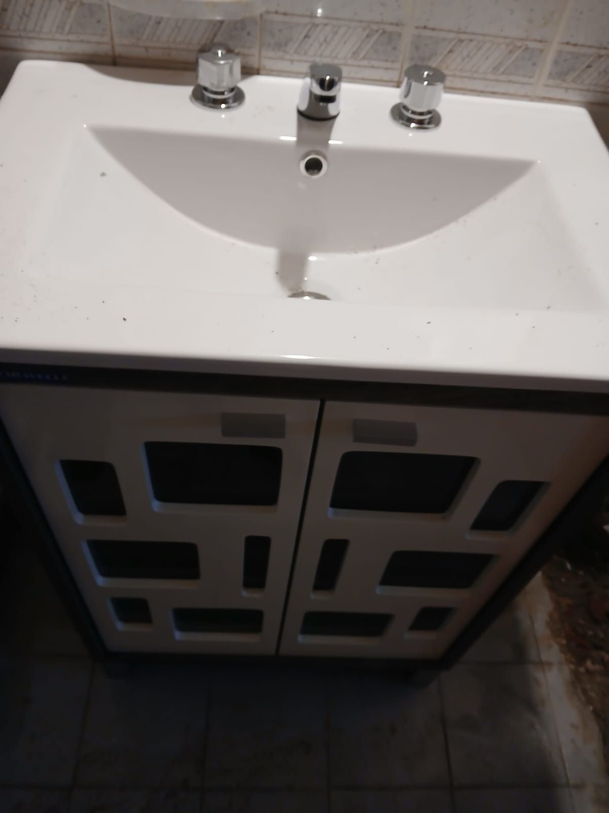 Lavabo de baño blanco con accesorios cromados, colocado encima de un mueble con recortes geométricos en las puertas.