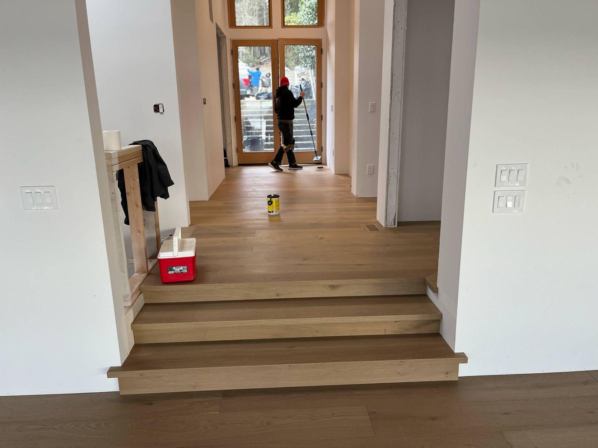 A man is standing in the hallway of a house cleaning the floor.