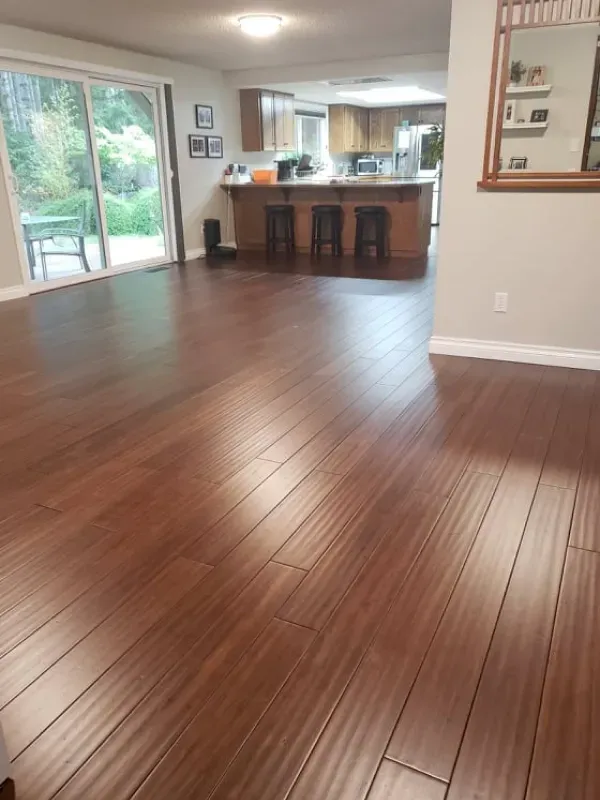A living room with hardwood floors and a kitchen in the background