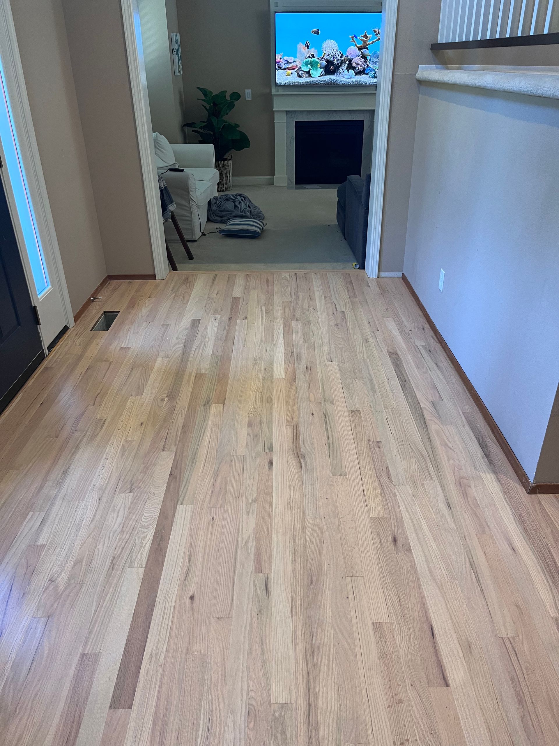 A wooden floor in a hallway leading to a living room.
