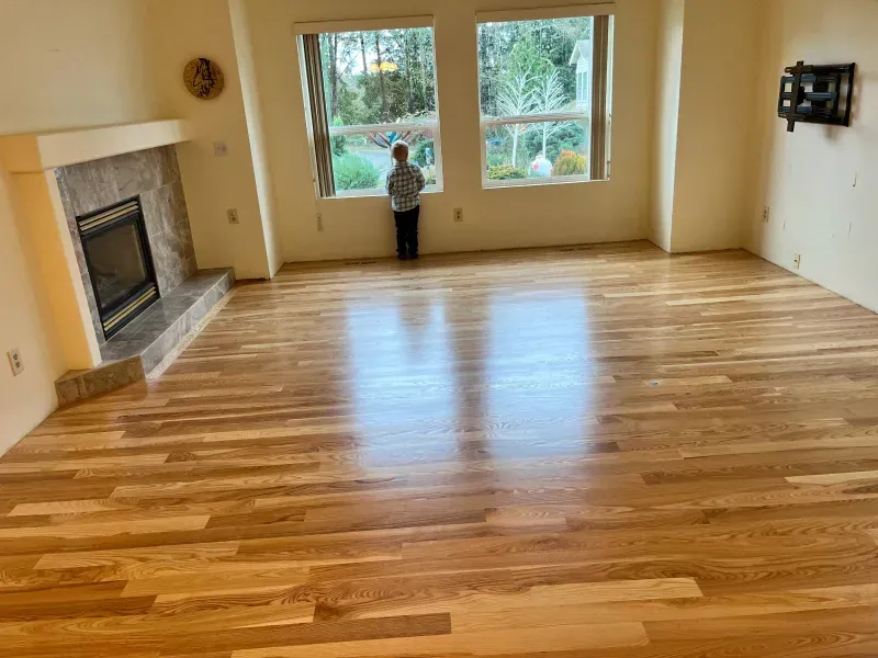 A boy is standing in a living room with a wooden floor and a fireplace.