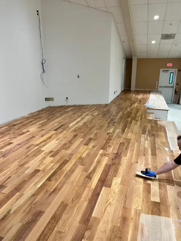 A man is polishing a wooden floor in an empty room.