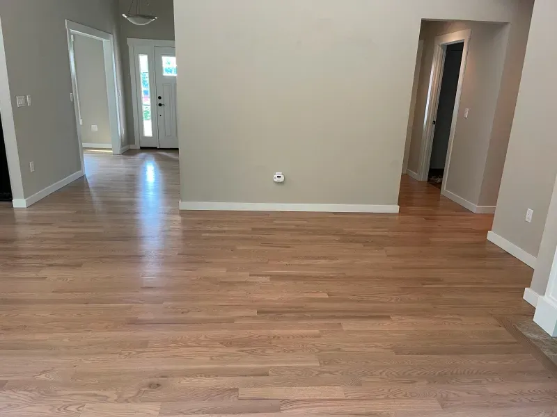 An empty living room with hardwood floors and beige walls.