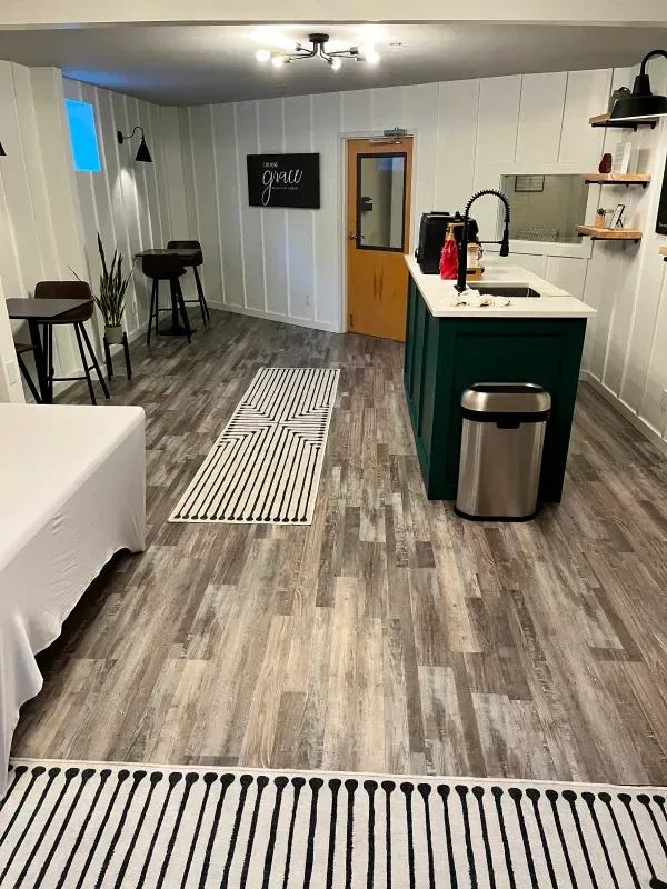 A kitchen in a basement with wooden floors and a green island.