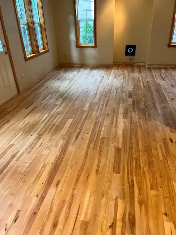 A living room with a wooden floor and two windows.