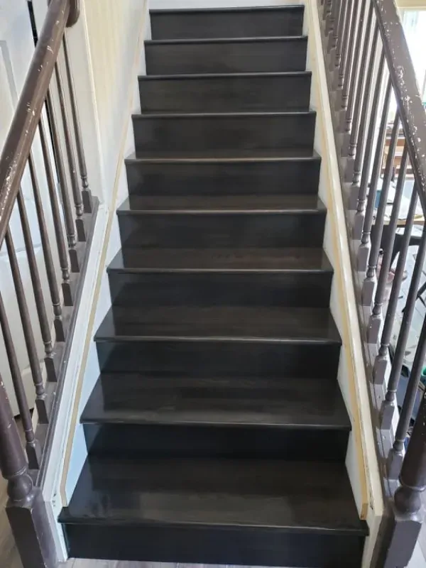 A set of black stairs with a wooden railing in a house.