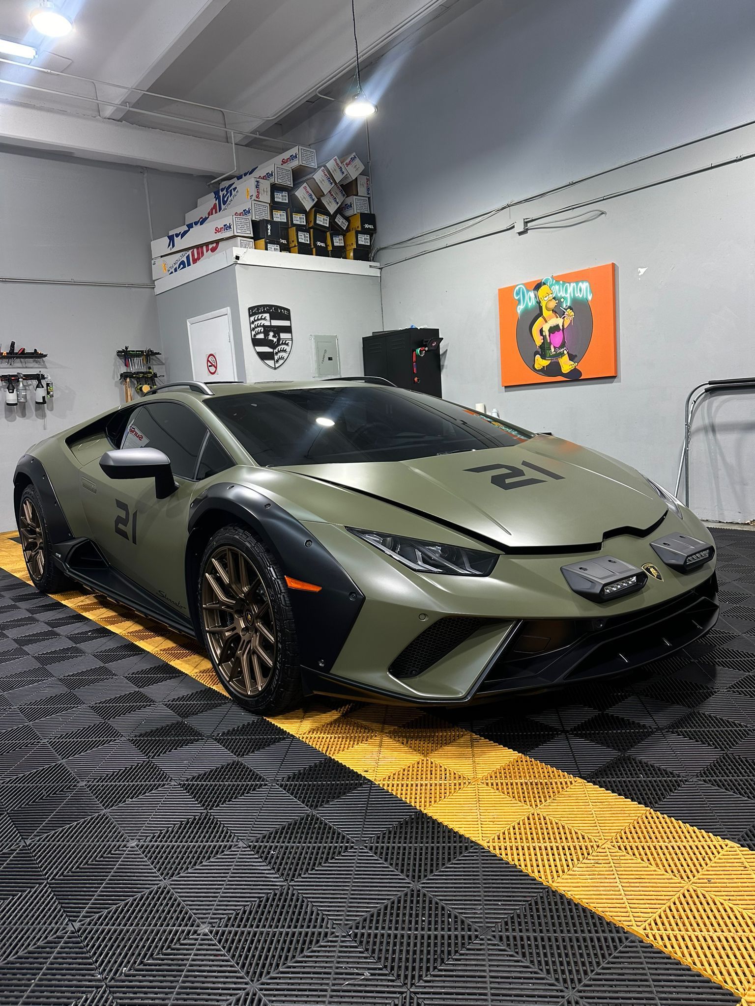 Olive green Lamborghini Huracan in a garage with yellow stripe, number 21 on the hood.