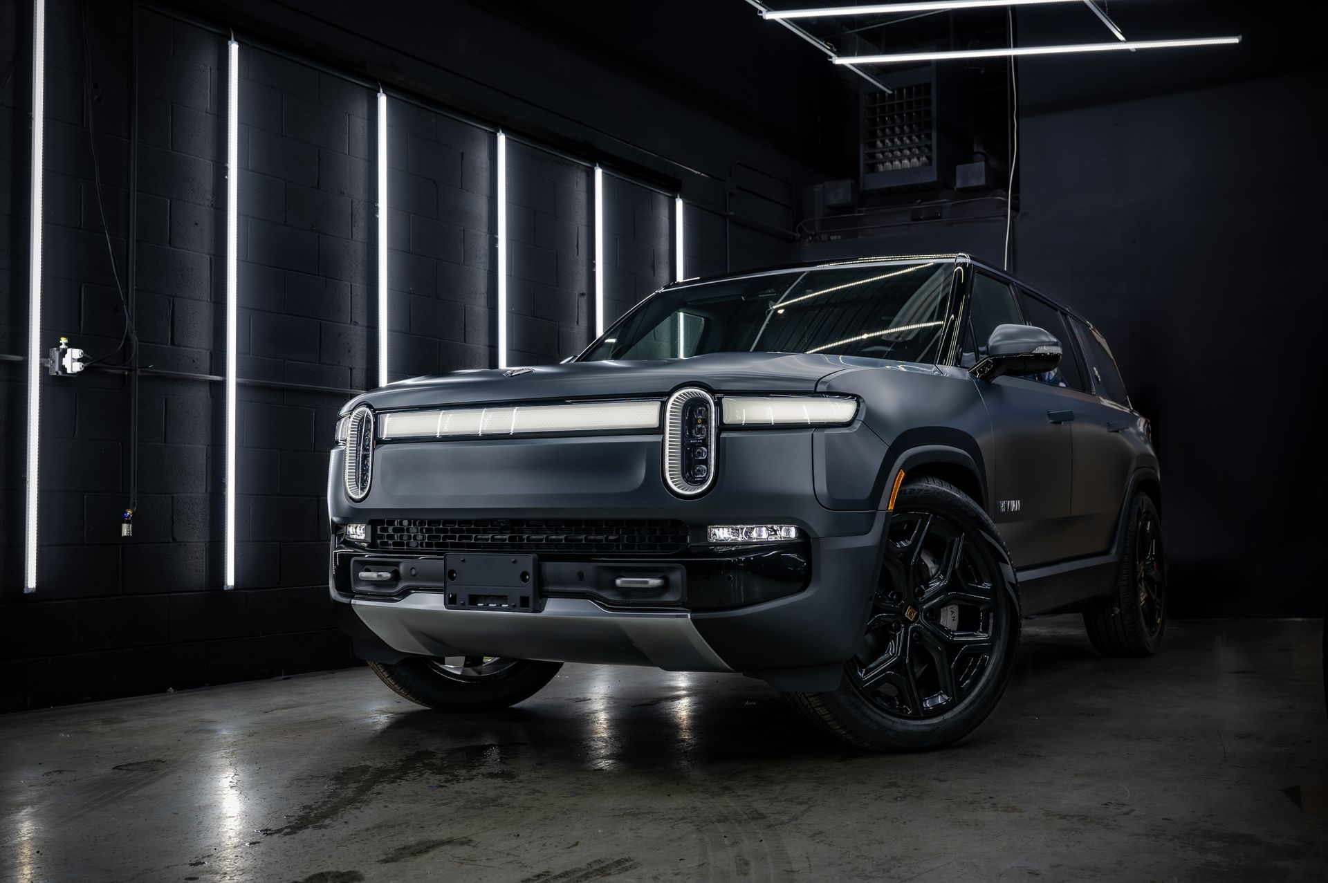 Gray Rivian electric SUV, in a dark studio with vertical lights.