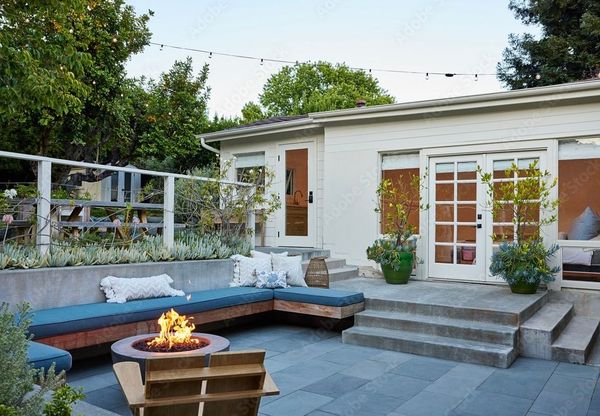 Modern backyard patio with fire pit, blue sectional seating, and white house with steps and French doors