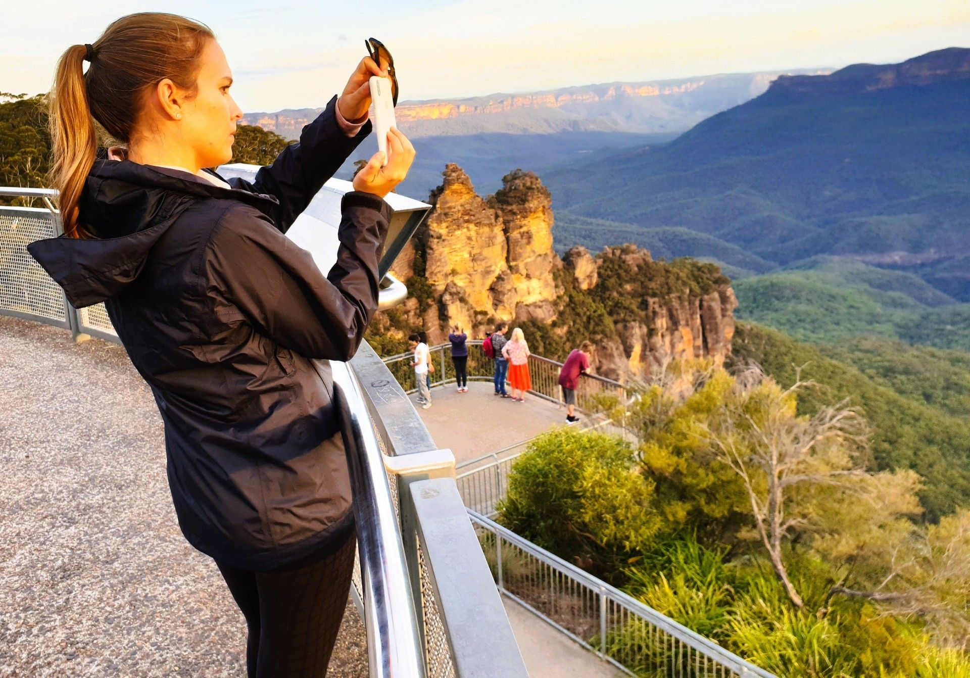 A woman is taking a picture of a mountain with a cell phone.
