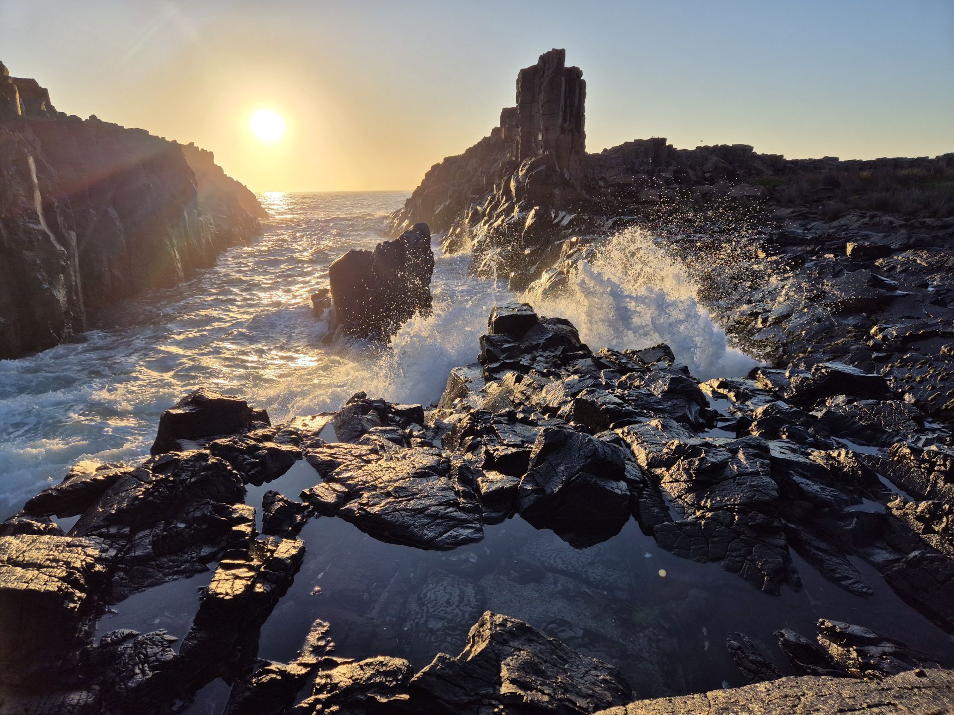 The sun is setting over the ocean and the waves are crashing against the rocks