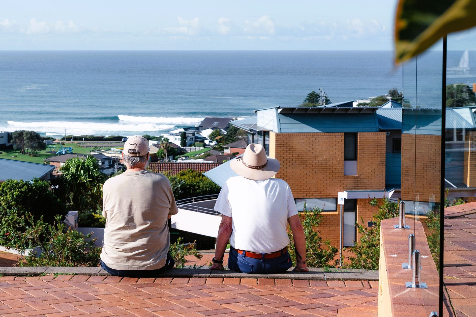 Two people taking photos of a koala eating eucalyptus leaves on a branch in a zoo enclosure.