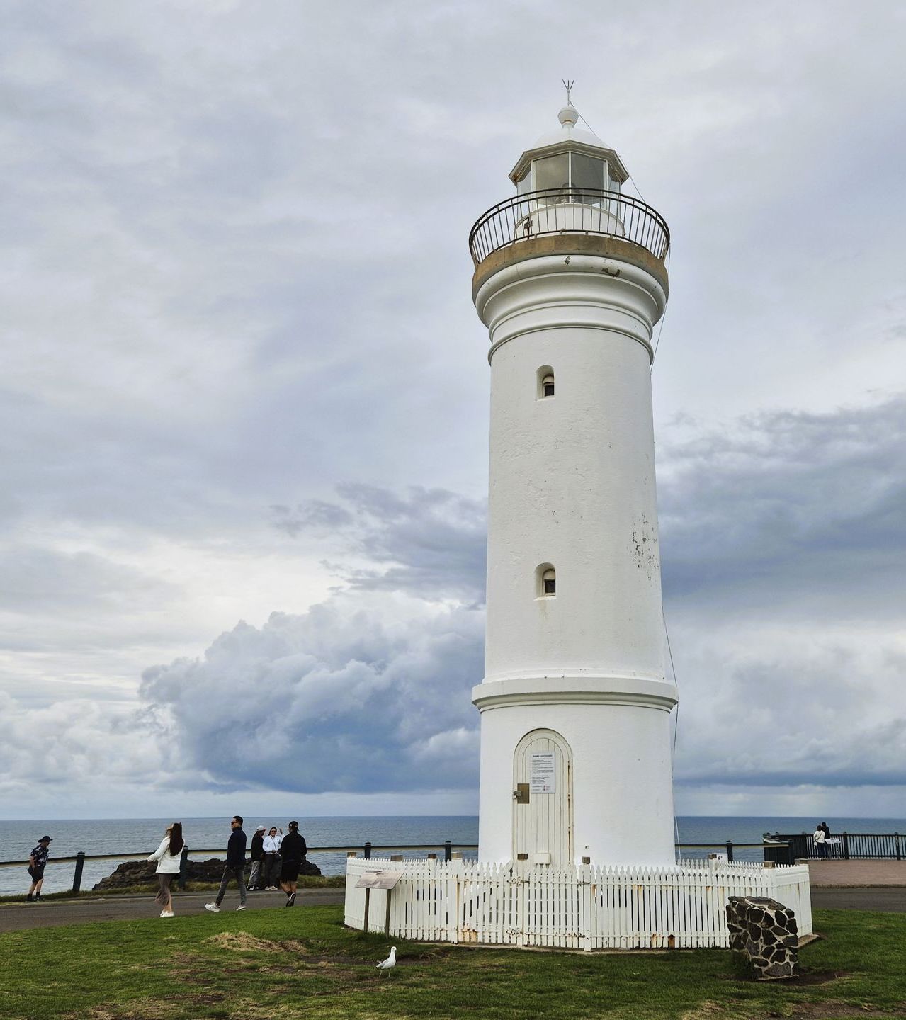 A white lighthouse is sitting on top of a lush green field next to the ocean.