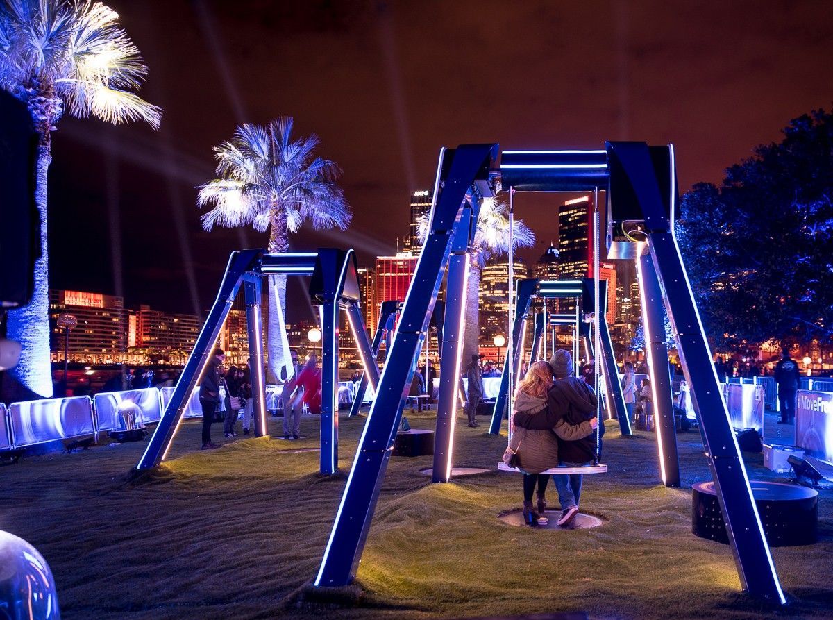 A couple is sitting on a swing in a park at night.