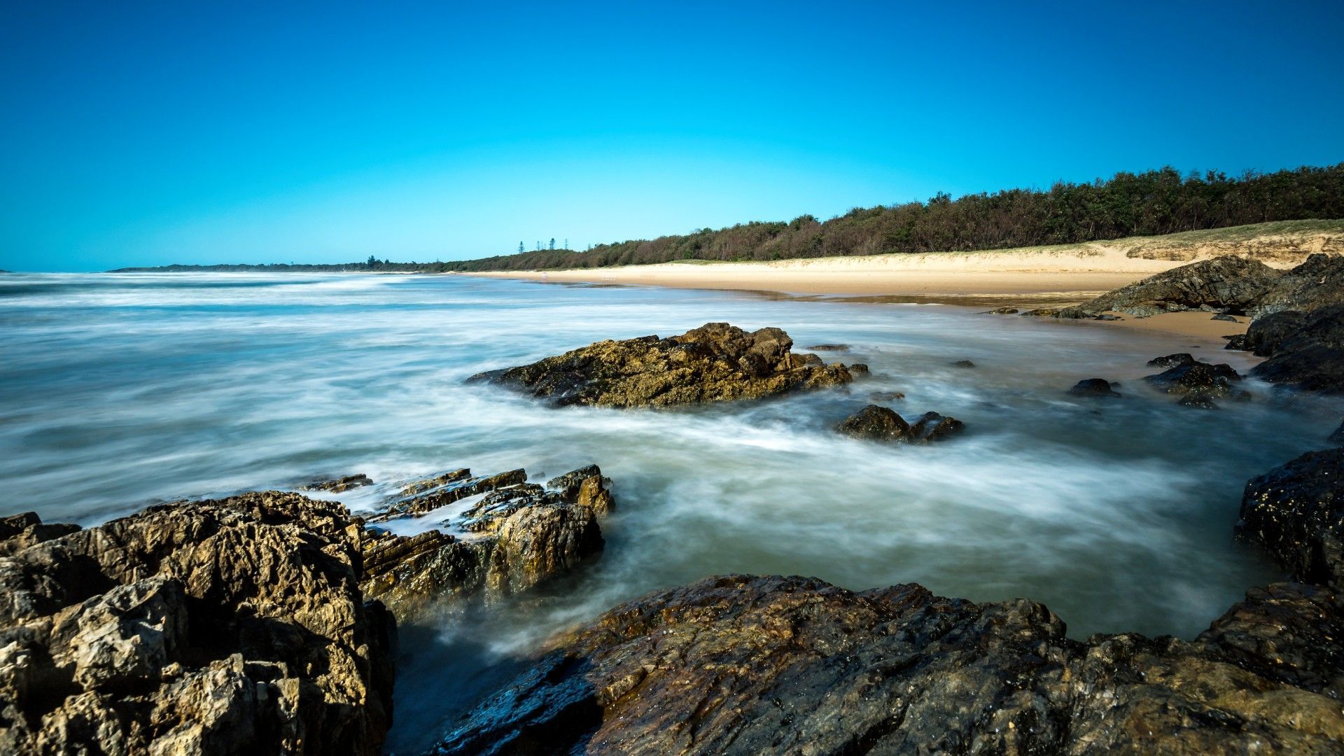 A long exposure photo of a beach with rocks and waves coming in.