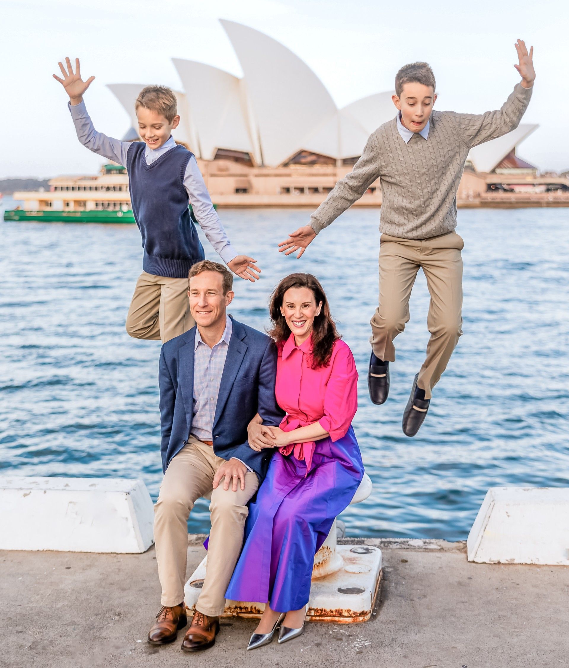 A family is posing for a picture in front of the opera house in sydney.