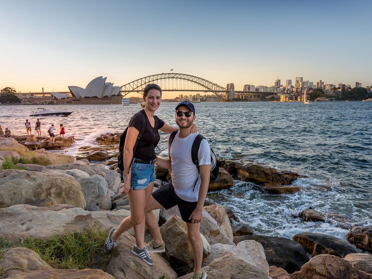 A man and a woman are standing on rocks near the water.