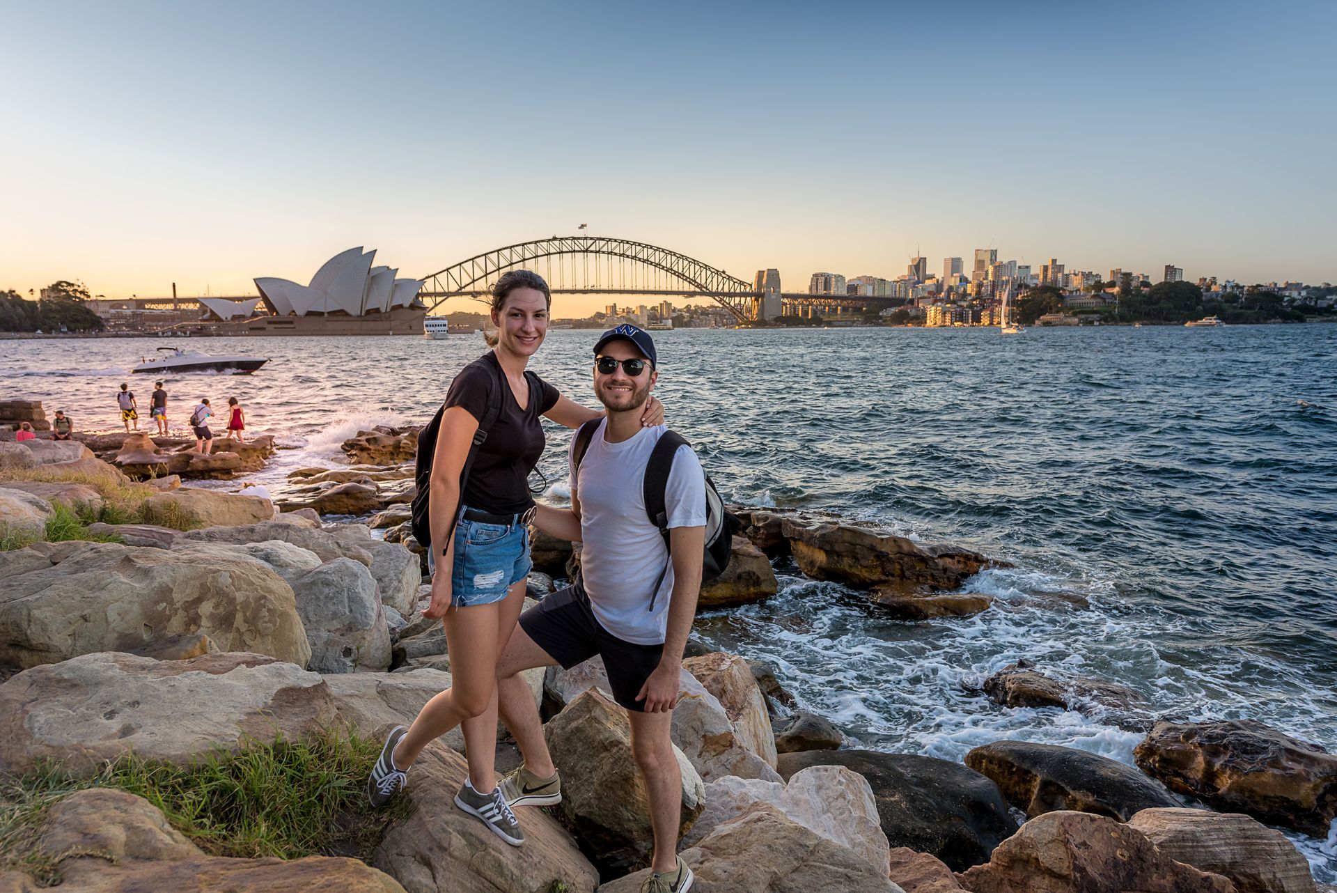 Two people pose by the river with the Sydney Opera House behind them