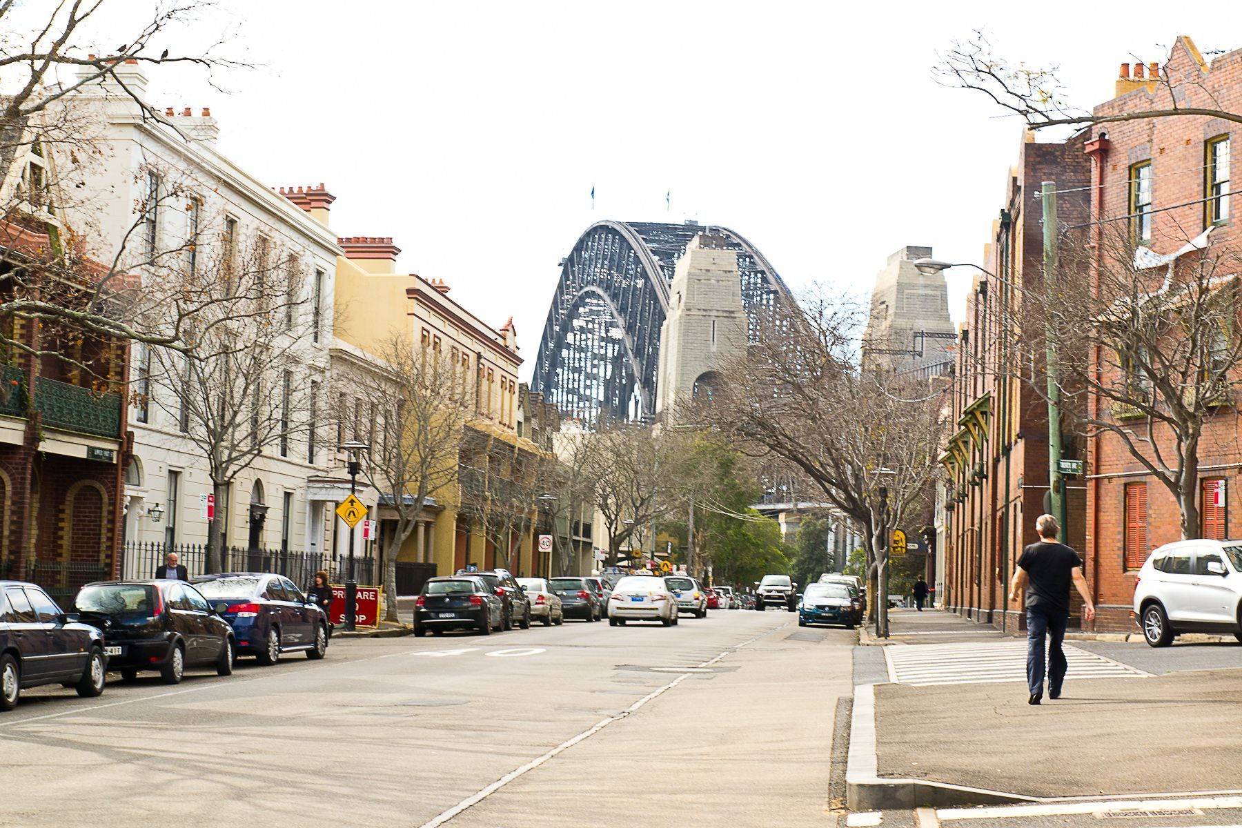 A man is walking down a street with a bridge in the background.