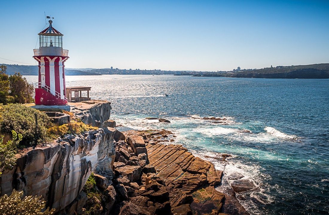 A red and white lighthouse is sitting on top of a rocky cliff overlooking the ocean.
