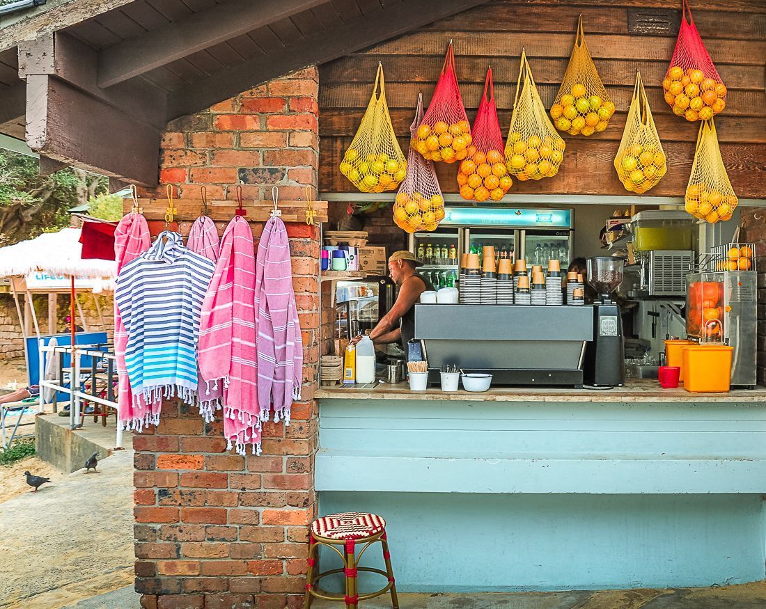 A man is standing behind a counter in a restaurant with a bunch of fruit hanging from the ceiling.