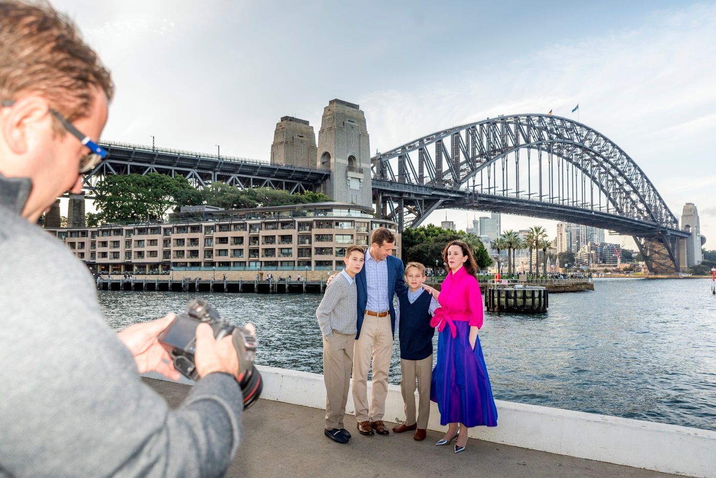 A man is taking a picture of a family in front of the sydney harbor bridge.
