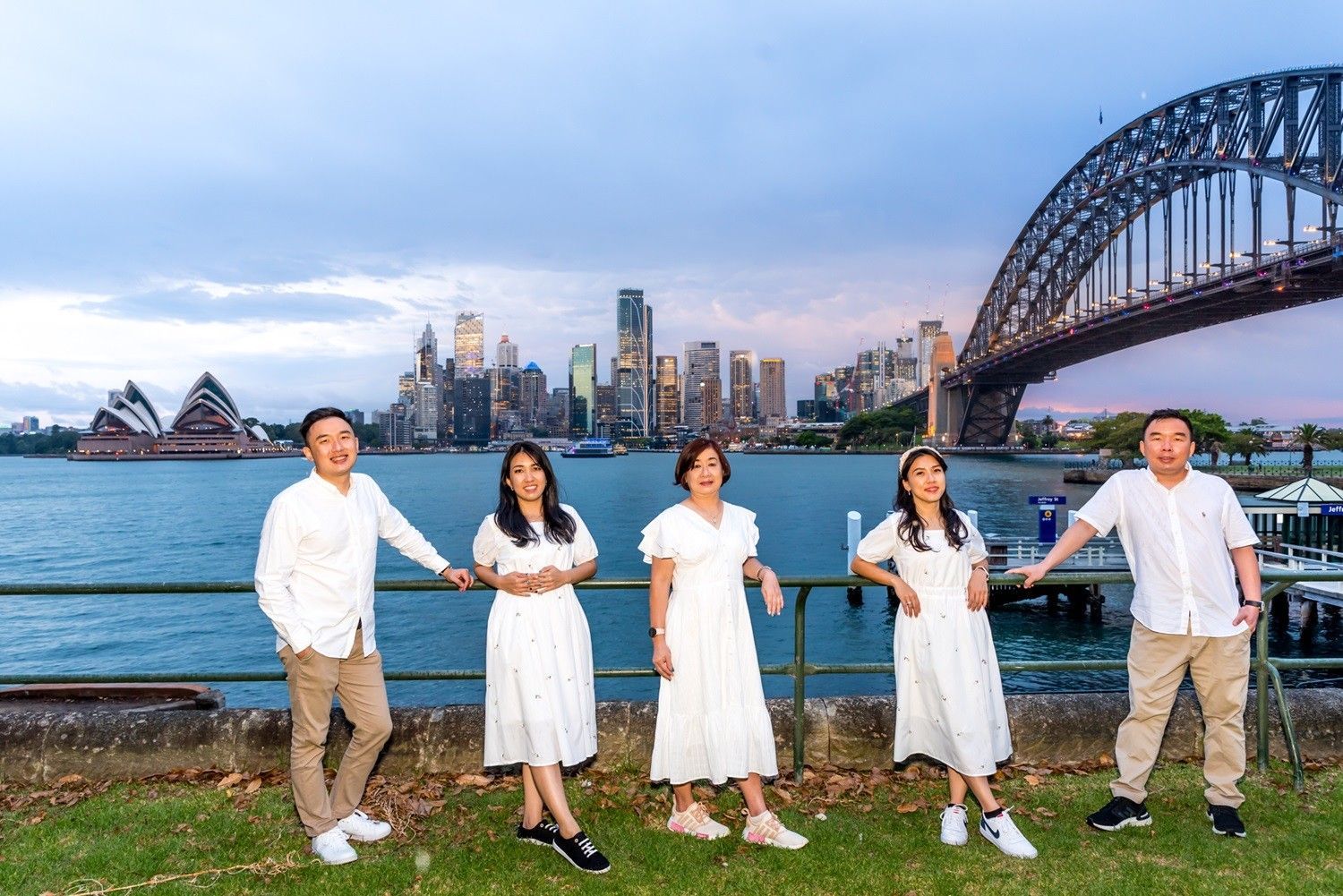 A family is posing for a picture in front of the harbor bridge in sydney.
