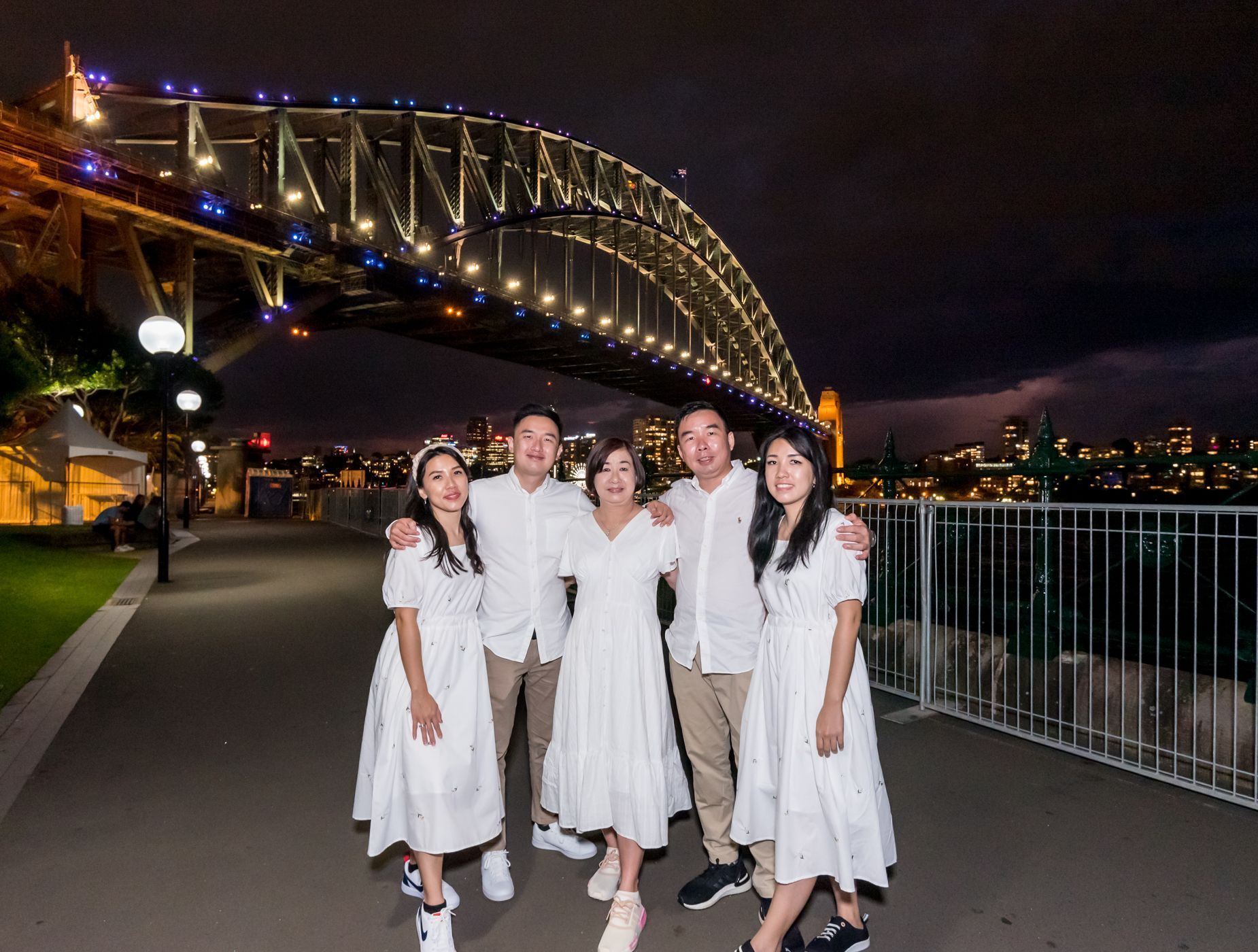 Family poses under Sydney Harbour Bridge at night. All wear white clothing.