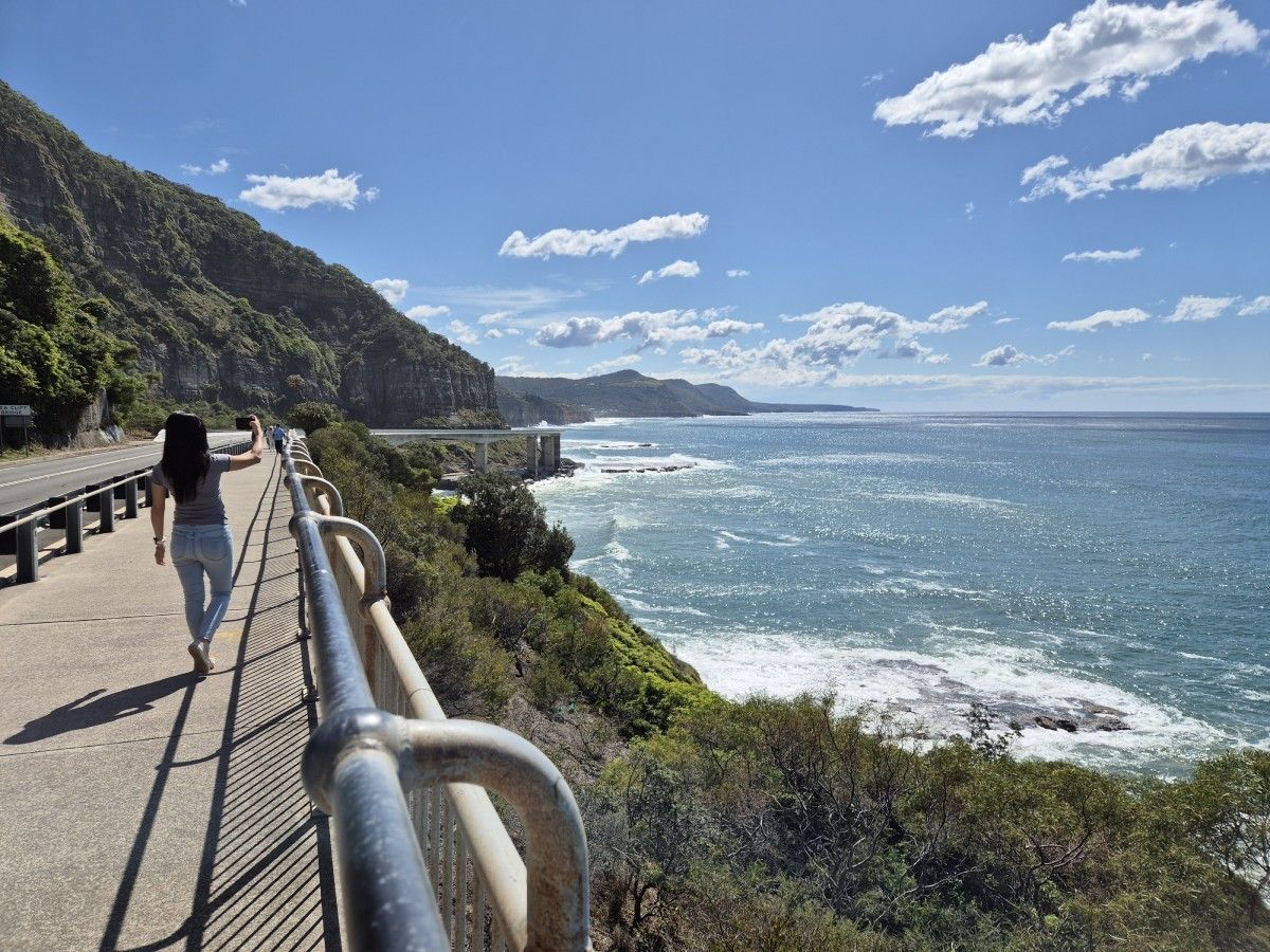 A woman is walking on a path overlooking the ocean.