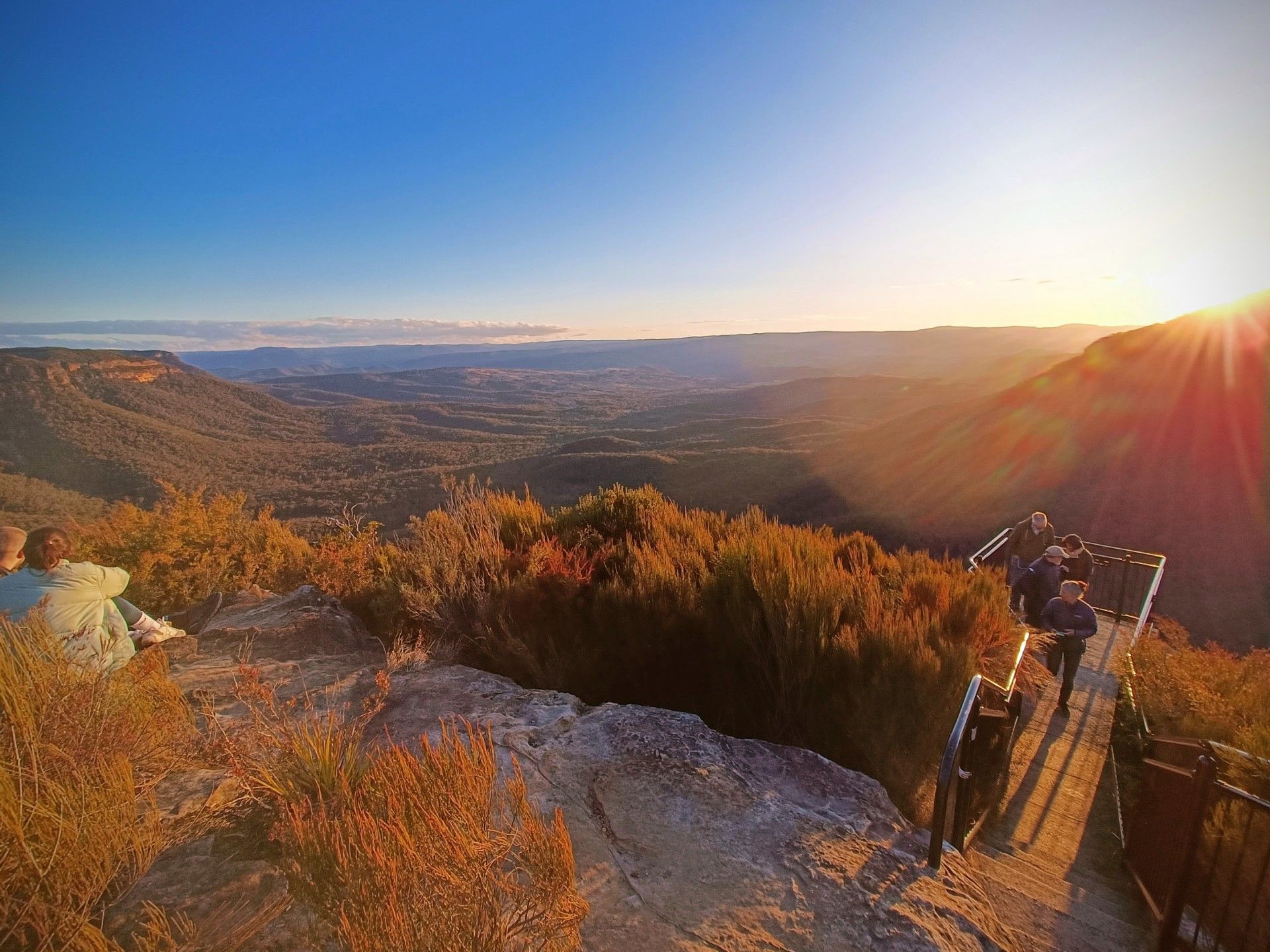A group of people are sitting on top of a mountain looking at the sunset.