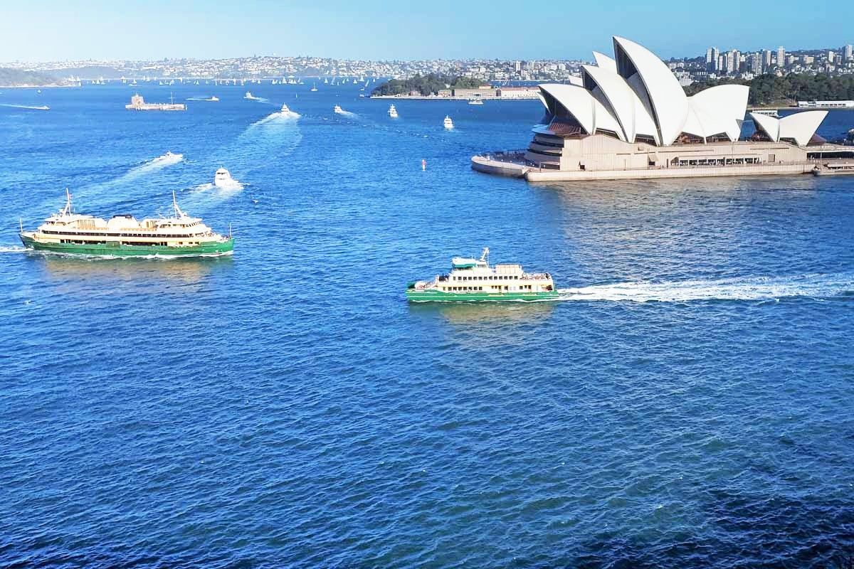 A group of boats are floating in the water near the opera house in sydney.