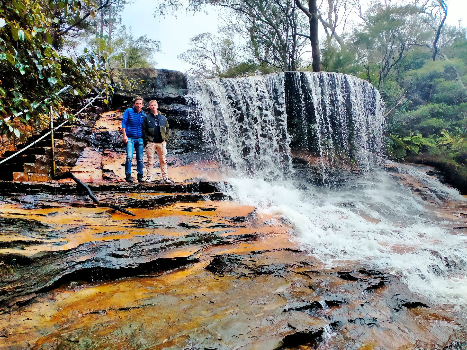 Two men are standing in front of a waterfall.