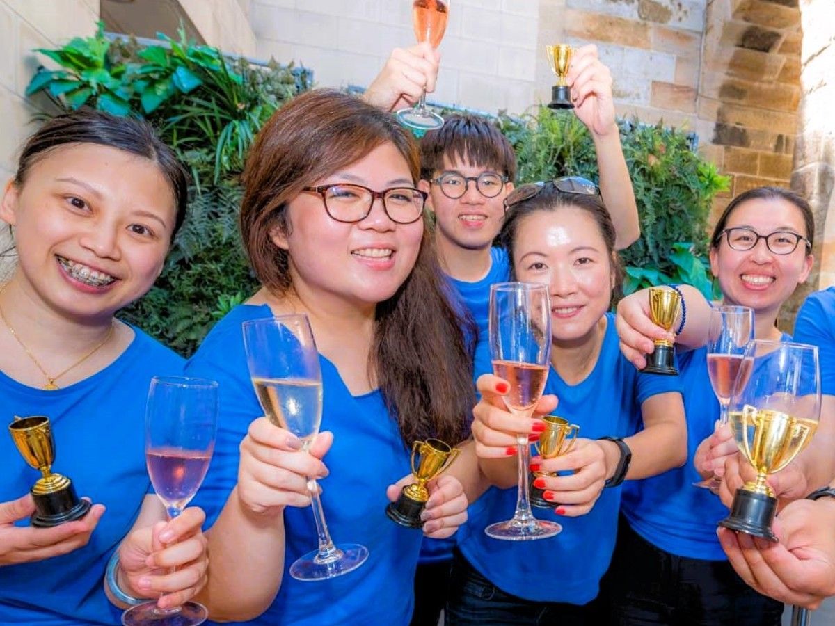 A group of people in blue shirts are holding champagne glasses and trophies.