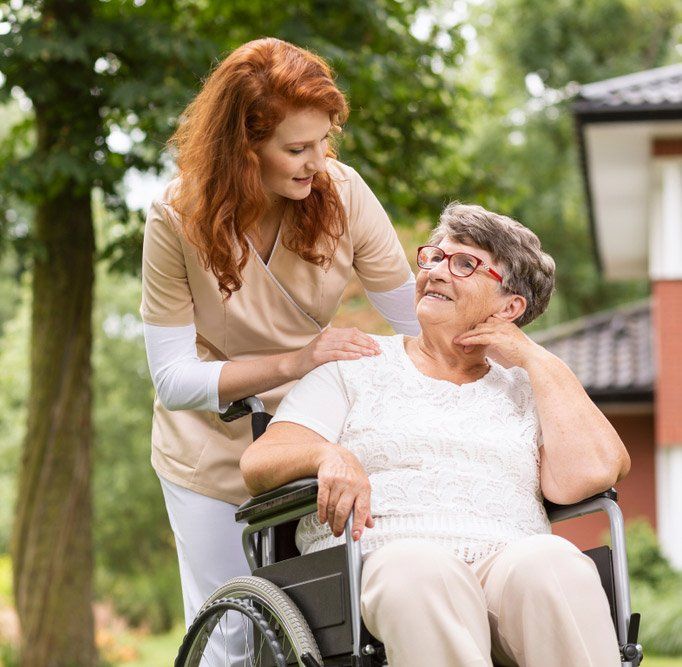 A Female Carer Helping An Elderly Woman In A Wheelchair In The Garden — iCan Support Services Kawana QLD