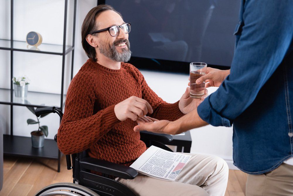 A man in a wheelchair is getting a glass of water from another man — iCan Support Services Kawana QLD