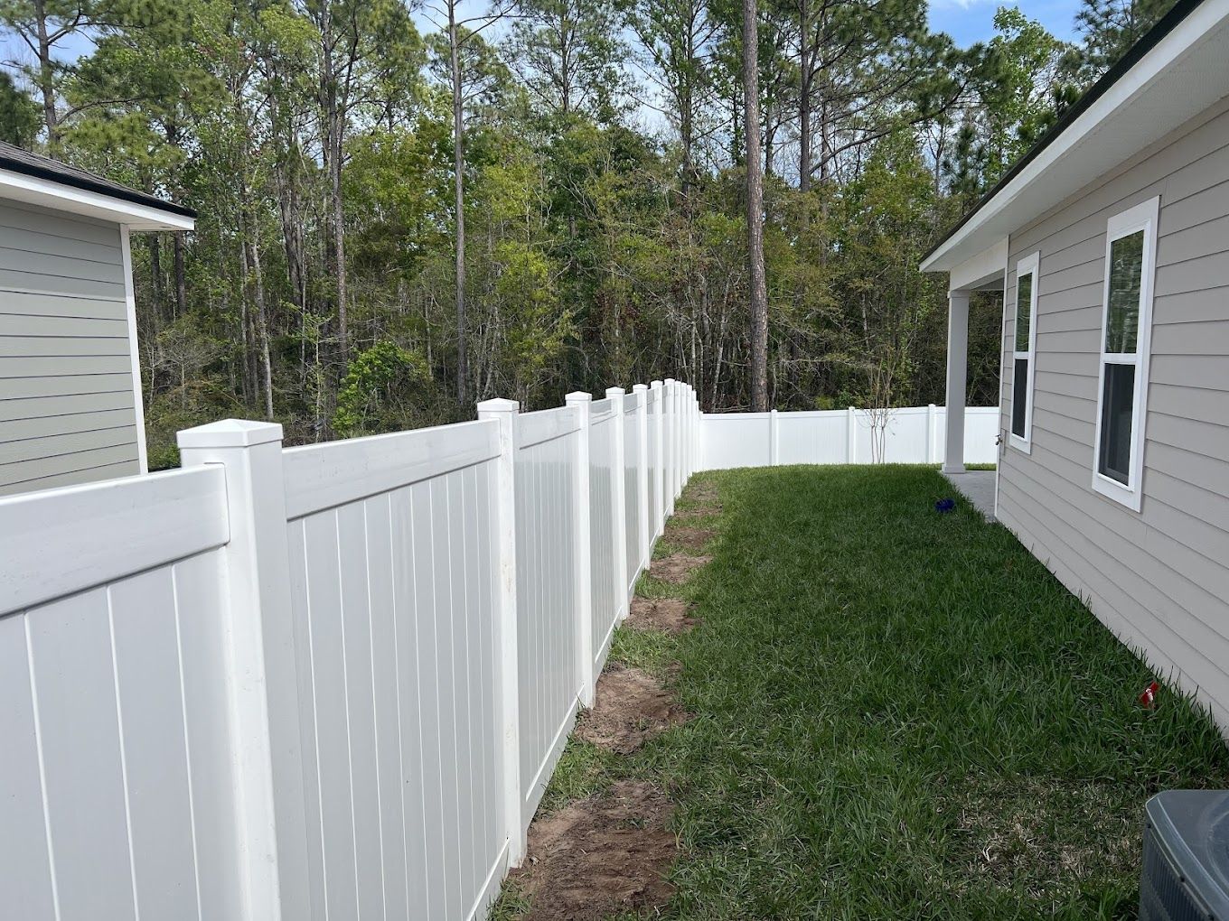 A white fence surrounds the backyard of a house.