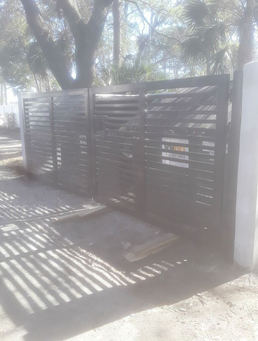 A black gate is sitting on the side of a road next to a tree.