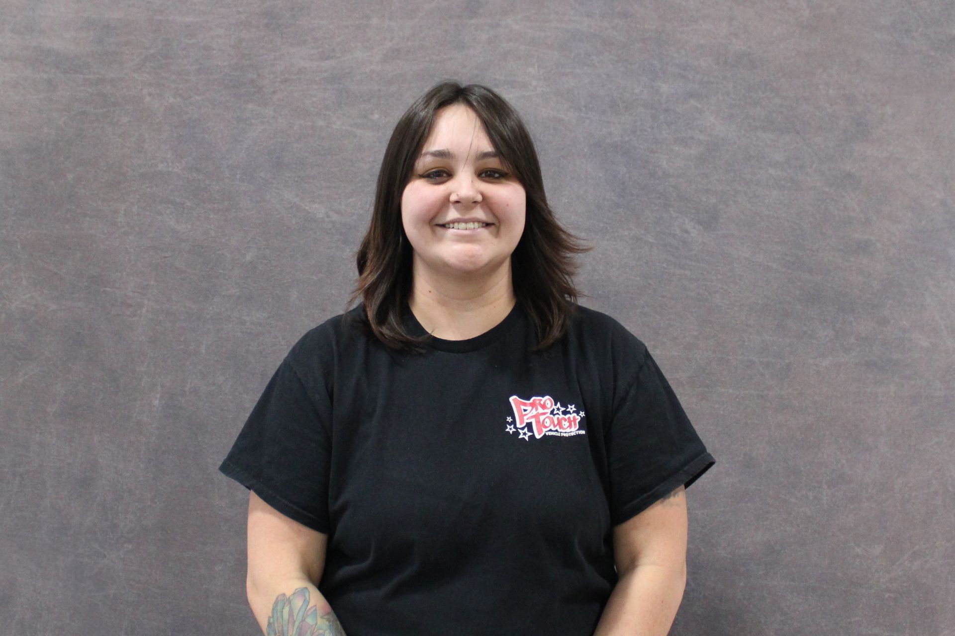 Woman in black hoodie smiles in front of a gray background.
