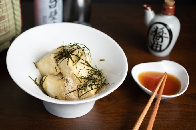 A bowl of Agedashi tofu next to a bowl of dipping sauce and chopsticks.